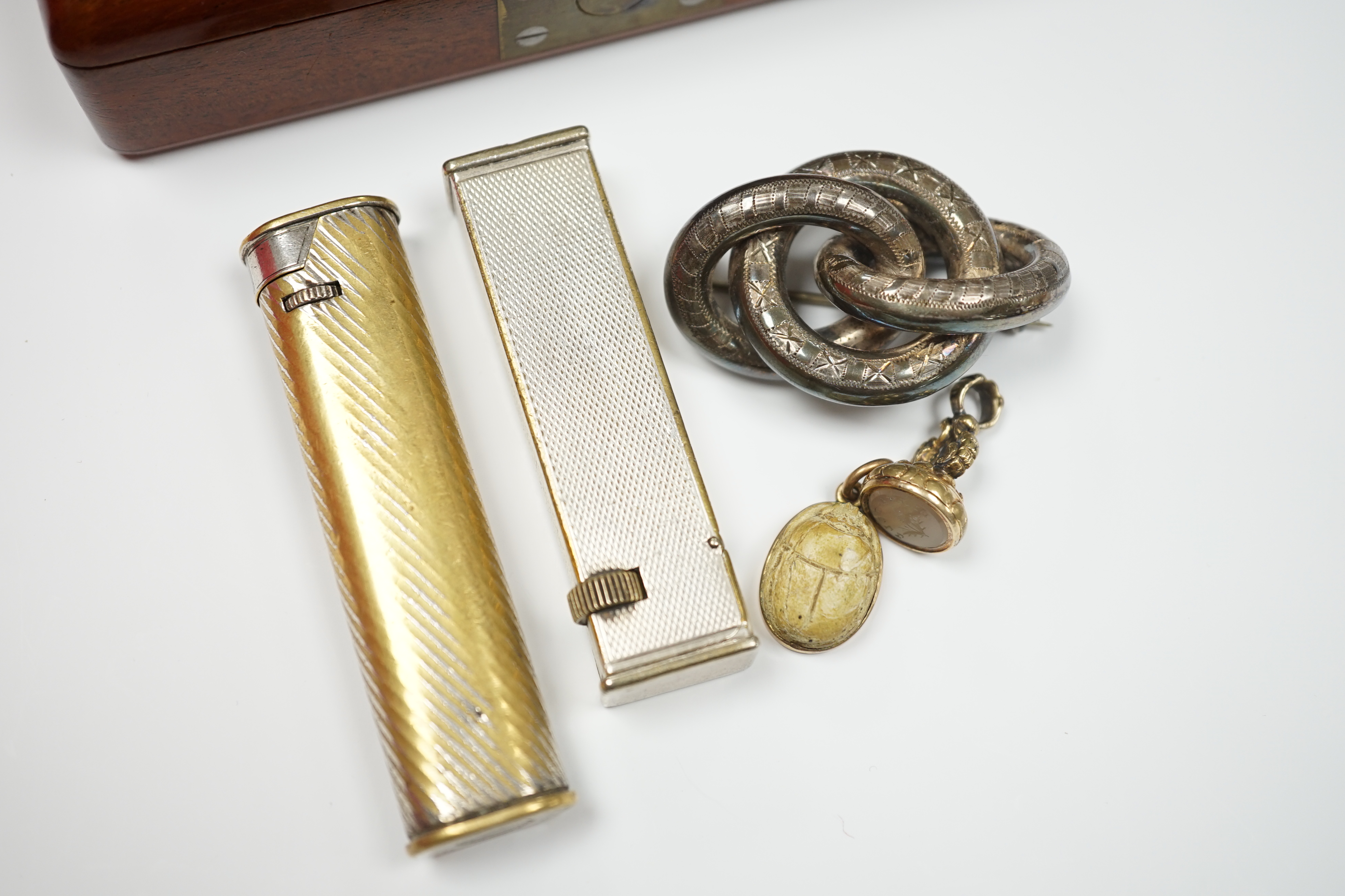 Two Dunhill lighters, largest 72mm, a yellow metal mounted scarab pendant, a gold plated and white carnelian set fob seal, the matrix carved with thistle and the phrase 'Dinna Tell', an engraved white metal knot brooch a